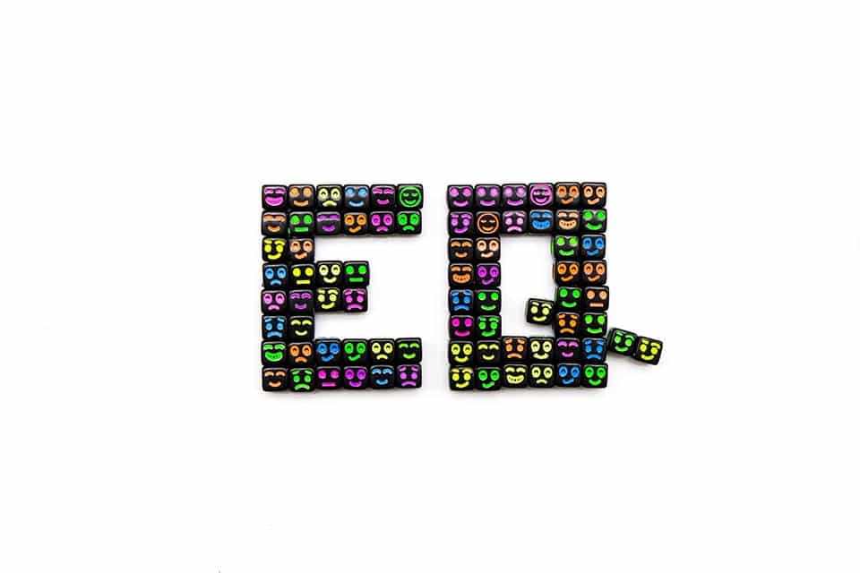 The letters E and Q in capital letters on a white background. Each letter is black, but they each are spotted with a variety of emojis of different facial expressions which are conveying a variety of emotions