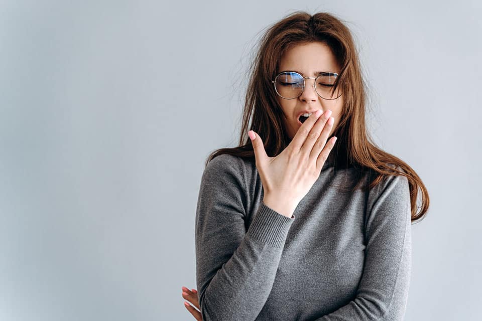 Woman sleepy tired girl yawning is experiencing sleep deprivation. Health balance sleep deprivation concept. Female student or worker with lack of slumber on gray background.